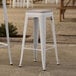 Two white Lancaster Table & Seating outdoor backless bar stools with gray fabric cushions on a patio.