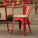 A red Lancaster Table & Seating outdoor arm chair with a tan cushion at a table on an outdoor patio.