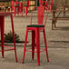 A red Lancaster Table & Seating outdoor cafe barstool with a black cushion on a patio.