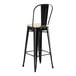 A black Lancaster Table & Seating outdoor cafe bar stool with a tan cushion.