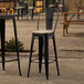 A Lancaster Table & Seating black outdoor cafe barstool with a tan cushion on a table outdoors.