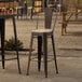 A Lancaster Table & Seating copper outdoor barstool with a tan cushion on an outdoor patio table.