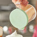 A person using a green Choice lid to sprinkle powder onto a cupcake.