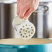 A hand using a clear plastic shaker lid to pour seasoning into a blue pot.