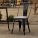 A black Lancaster Table & Seating outdoor cafe chair with a gray cushion sits on a patio.