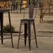 A set of three Lancaster Table & Seating metal outdoor cafe barstools with black fabric cushions.