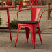 A red Lancaster Table & Seating outdoor arm chair with a black cushion on a patio.