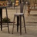 A Lancaster Table & Seating copper metal outdoor barstool with a gray cushion on a patio.
