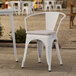 A white Lancaster Table & Seating outdoor arm chair with a gray cushion on a patio.