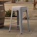 A gray metal outdoor backless counter height stool with a gray cushion on a stone surface.