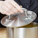 A hand holding a Vollrath Miramar metal pot lid over a silver pot.
