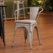 A Lancaster Table & Seating metal arm chair with a gray cushion on the seat.