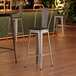 A Lancaster Table & Seating silver restaurant barstool with black fabric cushion on the seat and back.
