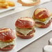 A row of King's Hawaiian Sliced Pretzel Slider Rolls with mini burgers on a white plate with fries.