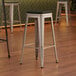 A Lancaster Table & Seating silver metal backless barstool with a black fabric cushion on the seat.