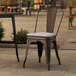 A Lancaster Table & Seating metal outdoor cafe chair with a gray cushion on a patio.