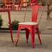 A red metal Lancaster Table & Seating outdoor cafe chair with a tan cushion on a patio.