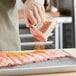 A person pouring medium ground seasoning from a Choice Polycarbonate Shaker onto a piece of meat.