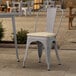 A Lancaster Table & Seating gray metal outdoor cafe chair with a tan fabric cushion on a patio.