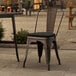 A Lancaster Table & Seating copper metal outdoor cafe chair with a black cushion on a patio.