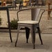 A Lancaster Table & Seating brown metal outdoor arm chair with a tan cushion on a patio.