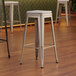 Lancaster Table & Seating silver metal backless barstools with gray fabric cushions on a black pole.