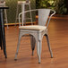 A Lancaster Table & Seating silver metal arm chair with a tan cushion.