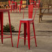 A red Lancaster Table & Seating outdoor cafe barstool with a gray cushion on a table in an outdoor patio.