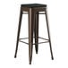 A brown metal Lancaster Table & Seating outdoor barstool with a black cushion.