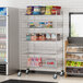 A Regency chrome metal retail display stand with shelves of snacks and drinks.