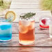 Arcoroc Essentials cooler glasses filled with blue, yellow, and red drinks on a wooden table.
