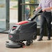 A woman using a Viper walk behind floor scrubber to clean a floor in a professional kitchen.