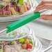 A person using a Baker's Mark green silicone bun / sheet pan clip to serve salad.