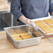 A woman wearing gloves holds a Vollrath stainless steel steam table pan full of food.