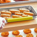 A person's hand using a yellow silicone tray clip to hold a tray of food.