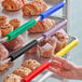 A hand using a red silicone clip to hold a rack of pastries on a Baker's Mark bun pan.