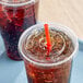 Two plastic cups with Choice clear plastic flat lids and straws on a table.