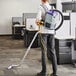 A man using a ProTeam GoFit backpack vacuum in a corporate office cafeteria.