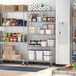 Regency chrome mobile wire shelving starter kit in a school kitchen with food items on the shelves.