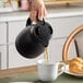 A person using a Zojirushi matte black stainless steel vacuum carafe to pour coffee into a white mug.