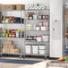 A Regency chrome wire shelving unit with 5 shelves holding food items in a large kitchen.