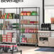 Regency black wire shelving with 4 shelves in a convenience store filled with beverages and boxes.