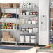 A Regency stainless steel mobile shelving starter kit in a large school kitchen with food items on the shelves.