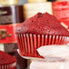 A hand in a white glove holding a red Hoffmaster fluted baking cup.