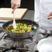 A person cooking food in a Vollrath stainless steel non-stick fry pan.