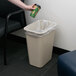 A hand pouring coffee into a Continental beige rectangular trash can.