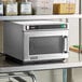 An Amana stainless steel heavy-duty commercial microwave on a stainless steel shelf.