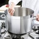 A chef stirring a large silver sauce pot.