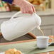 A person pouring coffee from a white Zojirushi glass carafe into a white mug.