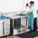 A man in a blue apron working on a stainless steel Regency dirty dishtable in a professional kitchen.